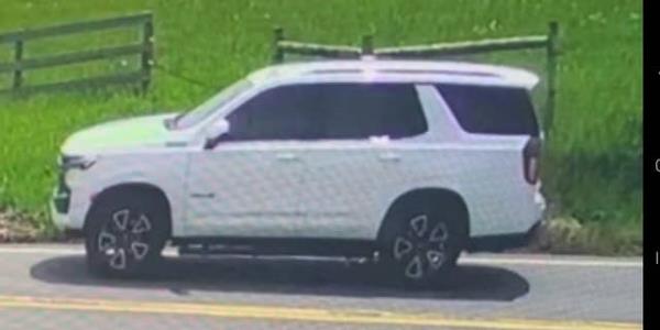 White SUV parked near wooden fence and grassy field