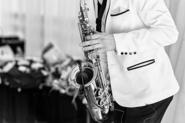 Saxopho<em></em>nist in white jacket plays the saxophone. Saxopho<em></em>nist jazz man with saxophone on wedding party