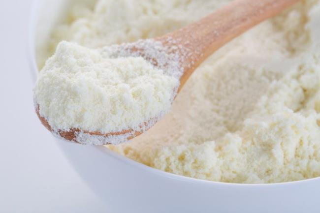 A bowl of milk powder and spoon. Close up.