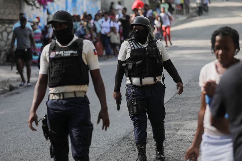 Police officers walk near people carrying their belo<em></em>ngings amid gang violence in Haiti's capital Port-au-Prince