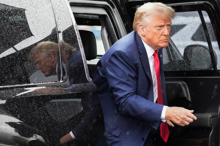 Do<em></em>nald Trump, dressed in a blue suit and red tie, exits a black vehicle with tinted windows.