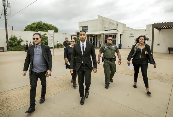 A photograph of John Legend, dream hampton, and others walking away from a prison.