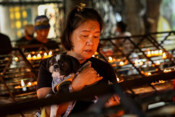 A woman praying in the Philippines. There are racks of small candles behind and in front of her