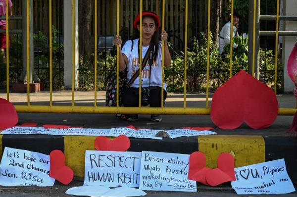 Pro-divorce protesters hold a rally in front of the Senate. One woman is standing behind yellow railings and holding o<em></em>nto them. The protesters have placed red hearts and placards around, One says human rights while another calls for second chances.