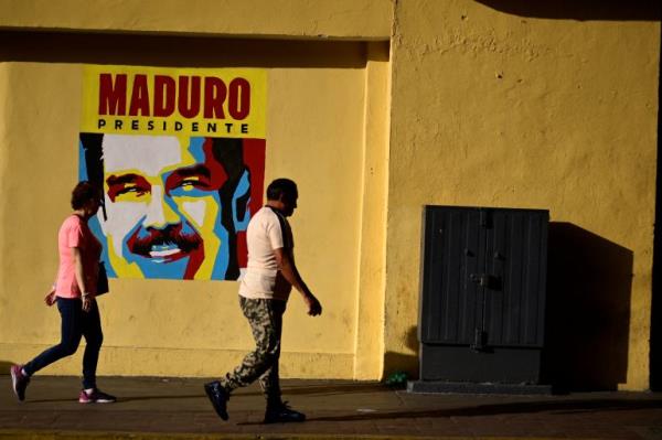 People walk past a poster of Nicolas Maduro