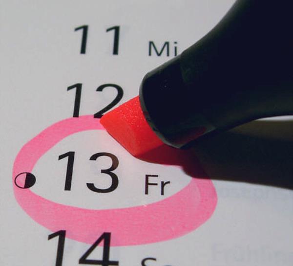 Point of highlighter pen drawing a bright pink circle around Friday 13 on a calendar.