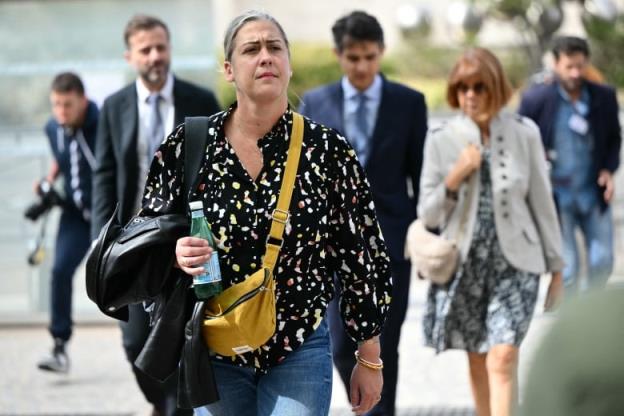 A woman in  a floral blouse and jeans walks toward a  camera