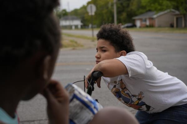 A kid leans on his bike handlebars as he gathers with neighborhood friends to sell Kool-Aid and Chips, Tuesday, Sept. 17, 2024, in Springfield, Ohio. Some were kept home from school because of the bomb threats at their schools, and if that happens again, they plan to be at the corner with Kool-Aid and chips again tomorrow. (AP Photo/Carolyn Kaster)