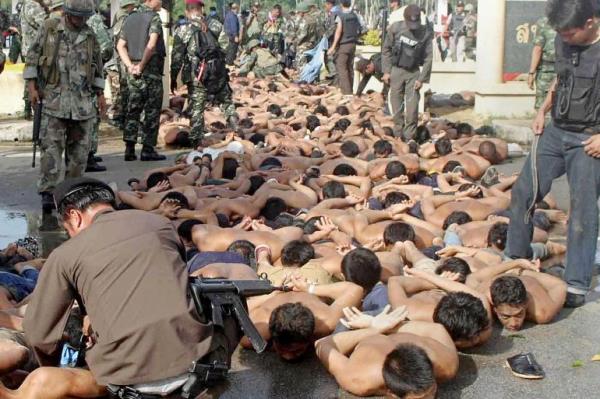 Protesters lying on the ground. Their hands have been tied behind their backs and they are bare chested. Thai soldiers and security perso<em></em>nnel are watching them.