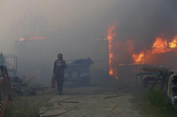 A man carries a fire extinguisher as he speaks on the phone while a me<em></em>talworking warehouse burns in Sever do Vouga, a town in northern Portugal that has been surrounded by wildfires, Monday, Sept. 16, 2024. (AP Photo/Bruno Fonseca)