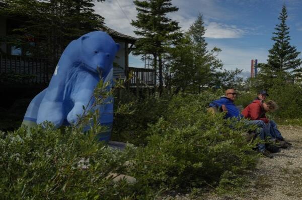 Tourists sit near a polar bear statue, Tuesday, Aug. 6, 2024, in Churchill, Manitoba. (AP Photo/Joshua A. Bickel)