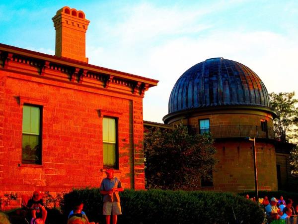 Red brick building next to domed building and people on the lawn.