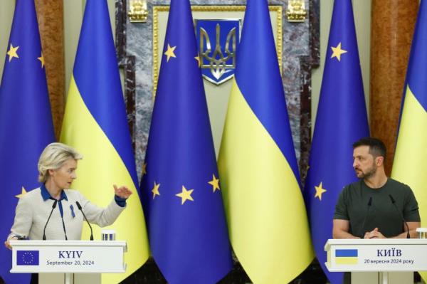 European Commission President Ursula von der Leyen and Ukrainian President Volodymyr Zelenskyy. They are standing at lecterns in front of Ukrainina and EU flags. Von der Leyen is gesturing with her hand. Zelenskyy is looking towards her. They look serious.