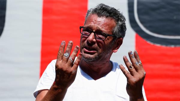 LoBaido speaks to reporters with paint on his hands in front of an American flag mural