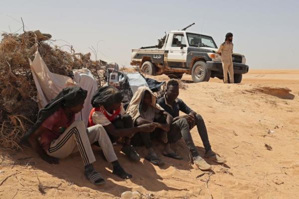 A Libyan border guard stands near migrants from sub-Saharan African countries who claim to have been abando<em></em>ned in the desert by Tunisian authorities without water or shelter, during a rescue operation in an uninhabited area near the border town of Al-Assah on July 16, 2023. Hundreds of migrants from sub-Saharan African countries were forcibly taken to desert and hostile areas bordering Libya and Algeria after unrest in early July in Sfax, Tunisia's second-largest city. (Photo by Mahmud Turkia / AFP)