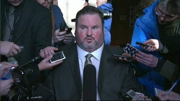 A man in a wheelchair faces reporters with micropho<em></em>nes in their hands.