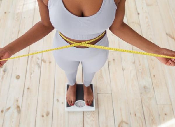 woman measuring waistline, on scale, co<em></em>ncept of tips to lose 10 pounds in one month