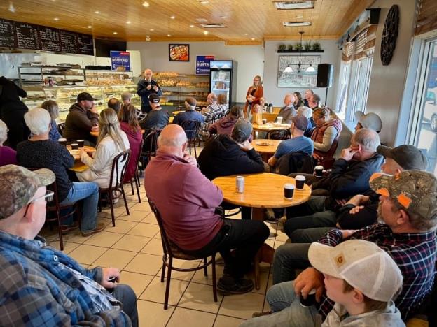 A man speaks to a crowd seated in a do<em></em>nut shop. 