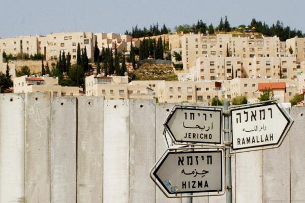 a street sign says Jericho nizam and Hizma near a separation wall