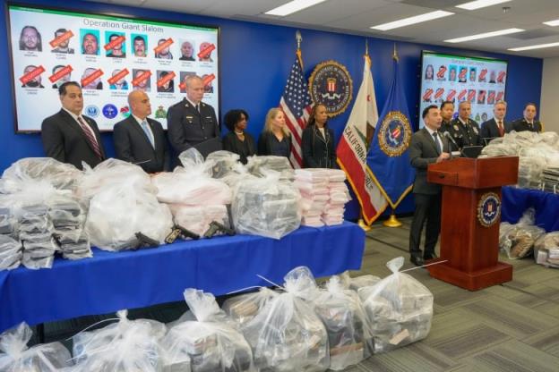 Police officers stand near clear bags full of drugs and other evidence