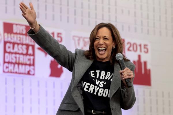 Kamala Harris waves as she speaks into a handheld mic, while wearing a T-shirt that reads "Detroit vs Everybody".