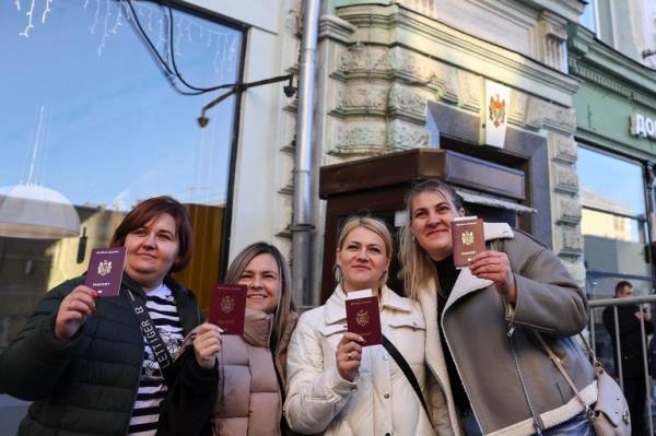 Women show their Moldovan passports while posing for a picture outside a polling station