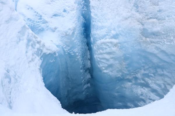 Deep layer of ice with large, very deep hole and thin stream of water flowing into the hole.