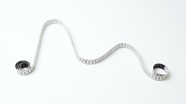 a white measuring tape curled into a graph-like curve with two peaks against a white background