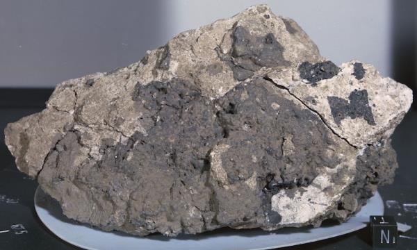 Irregular rock with made up of dark and light chunks, sitting on a blue plate.