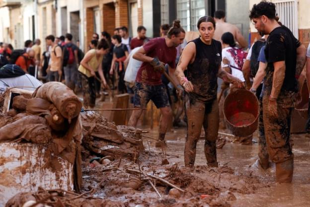 Volunteers partially covered in mud clean up after a flood.