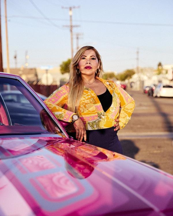 photo of woman looking proudly at camera and resting arm on side mirror of extremely shiny ornately painted pink car