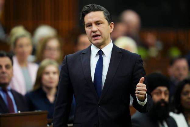 A man in a black suit motions with his hand as he speaks in the House of Commons.