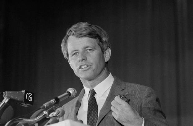 A black and white photo of a man speaking at a lectern.