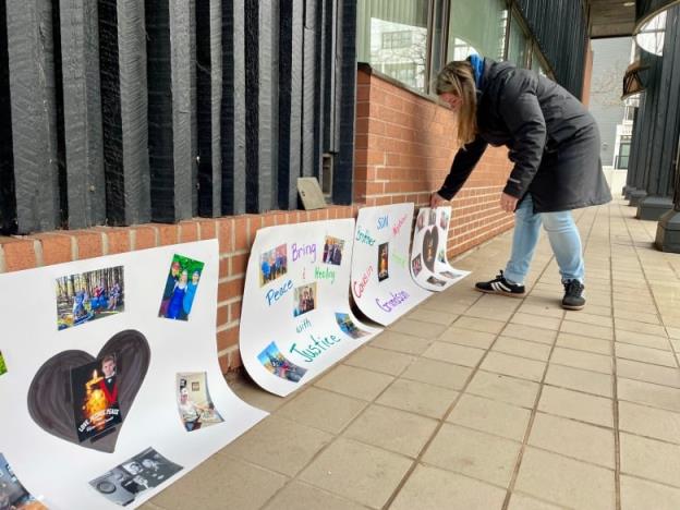 A woman places a row of signs with photos of a teenaged boy along the outside wall of a courthouse.