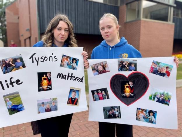 Sierra and Britney MacDo<em></em>nald hold up signs memorializing their brother Tyson outside the Supreme Court of Prince Edward Island.