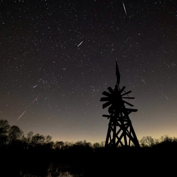 Starry sky with many white, short streaks coming from the center of the image, to the sides. There is a windmill in the middle, wher<em></em>e the streaks seem to separate.