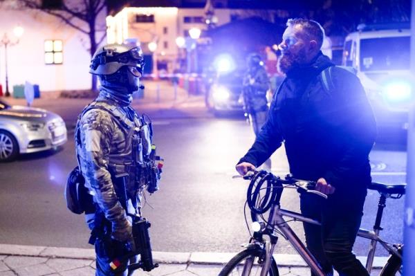 A police officer in tactical gear in Magdeburg speaks with a man wheeling a bike after a suspected attack on a Christmas market.