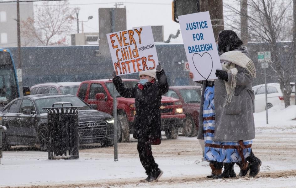 Community members carry signs in the snow. 