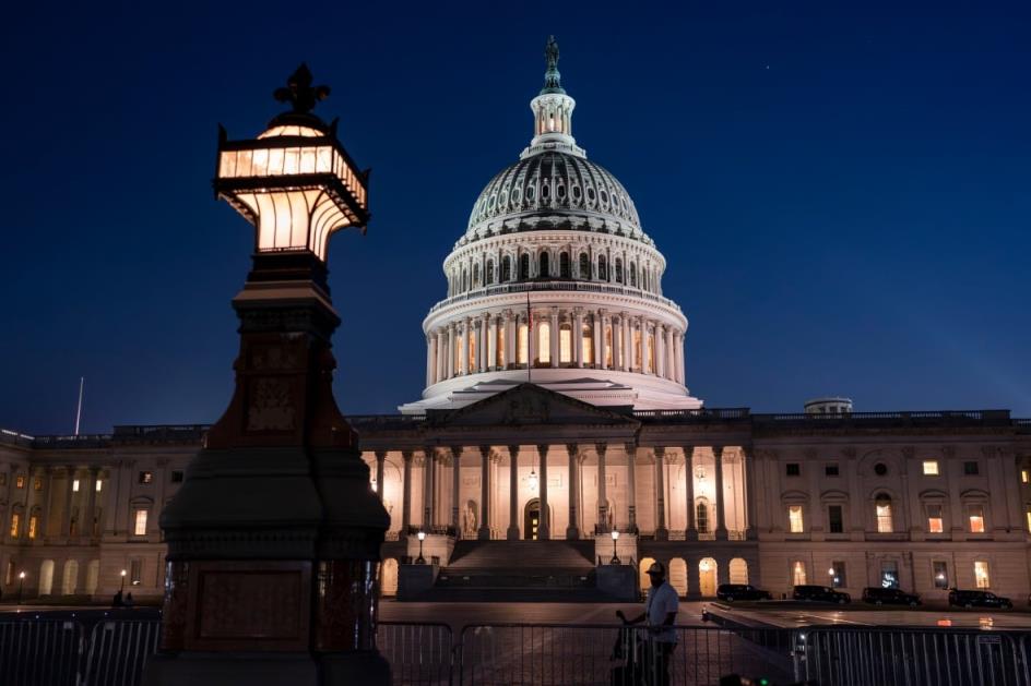 A large neoclassical building, lit from within, is pictured at night.