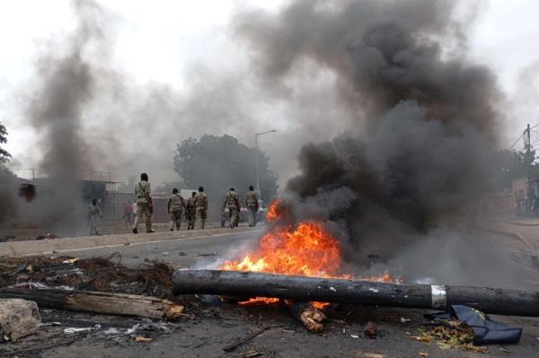 Pedestrians walk past a burning barricade in Maputo on December 24, 2024. - The capital of Mozambique was deserted on Tuesday, its main arteries heavily secured, noted AFP, the day after the co<em></em>nfirmation of the victory in the October elections of Frelimo, in power for half a century, while the opposition maintains his denunciations of fraud. Maputo remains frozen in a climate of fear and insecurity on Christmas Eve after violent demo<em></em>nstrations in the evening and night. The police, in armored vehicles, patrol the center. (Photo by Amilton Neves / AFP)