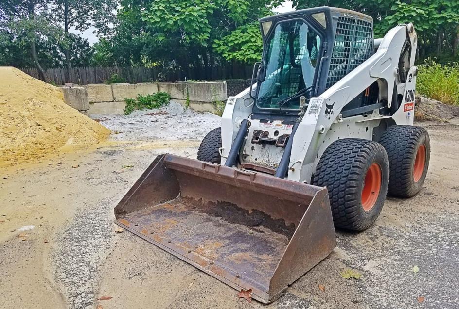 A skid-steer loader, which has large wheels, an enclosed cab and a shovel bucket on the front.