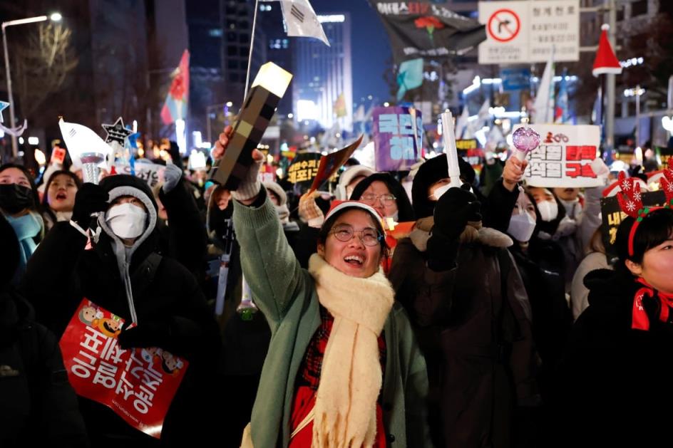 A woman wearing a green jacket and white scarf is pictured at the front of a crowd of protestors.