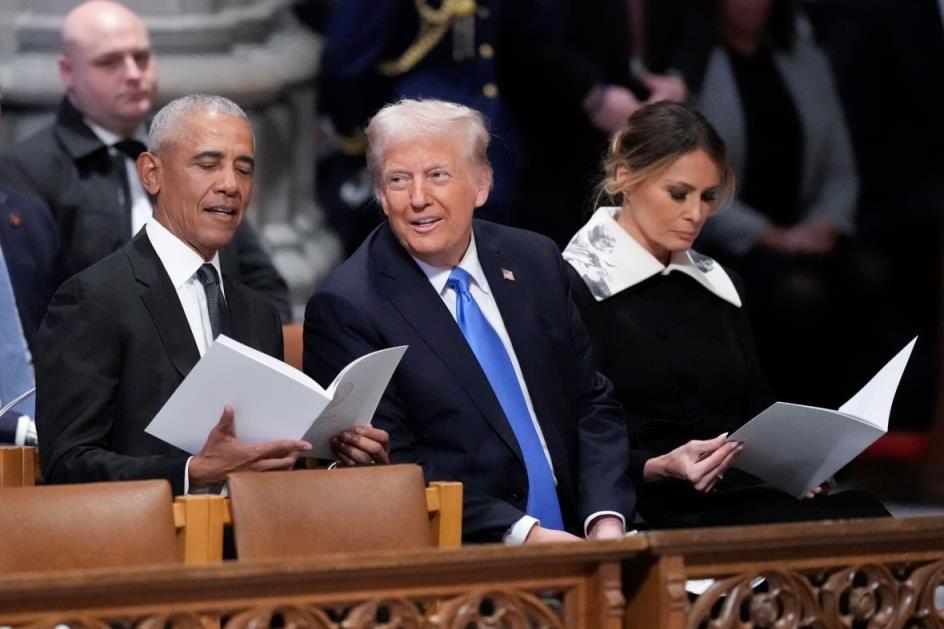 Two men, one Caucasian and one dark complected man are seated in suit and tie a church pew and appear to be in conversation. Beside the Caucasian man a Caucasian woman appears to be reading.