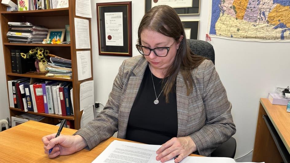 A woman sits at a desk in a jacket holding a pen a reviewing a court decision.