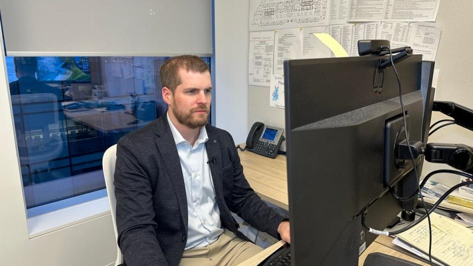 A man sits at a computer screen wearing a suit jacket and dress shirt.