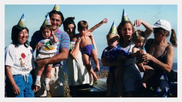 A group of people smile with kids wearing party hats 