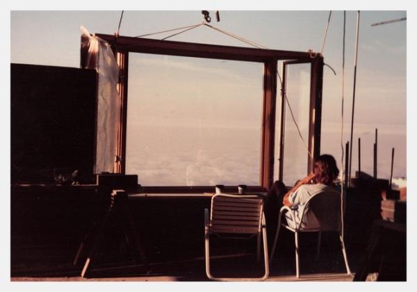 A man sits looking out a window at the clouds