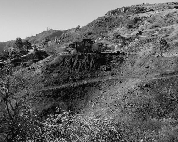 In a black and white photo there is a burned home on a mountain in Southern California