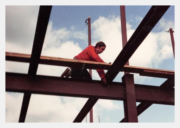 A man in a read sweatshirt works on building a house, as seen from below