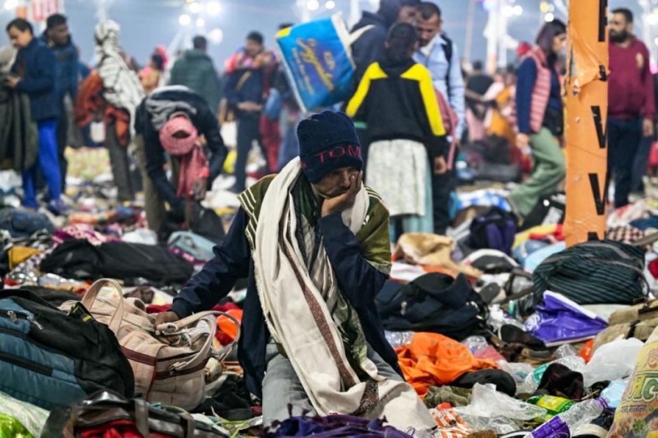 A person kneels surrounded by abando<em></em>ned bags and backpacks with people standing in the background.